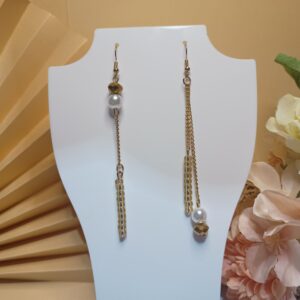 Brincos longos de pérola com cristais dourados, dispostos de forma assimétrica, correntes e miçangas douradas , com base anzol