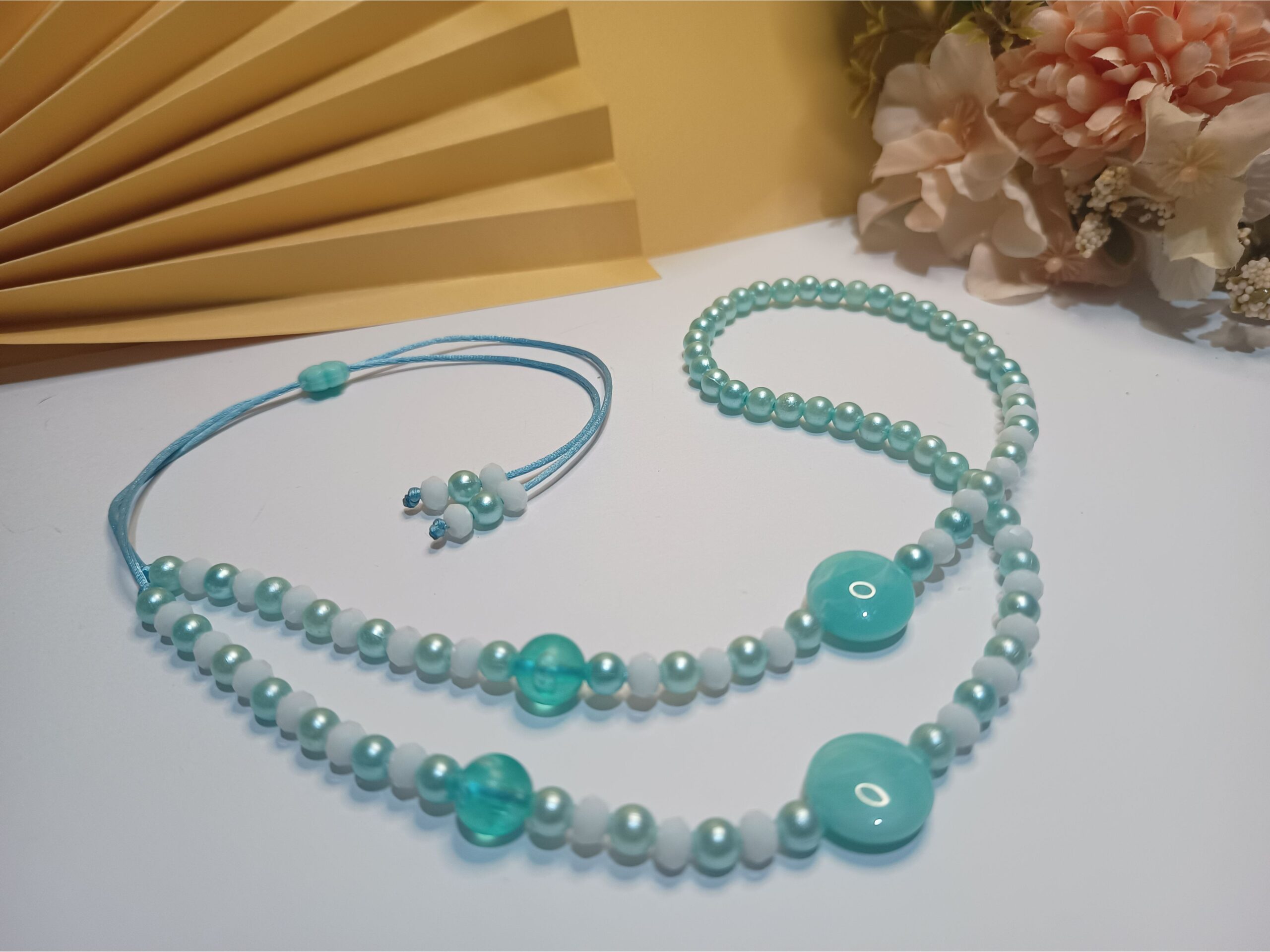 Conjunto Acqua com 3 peças, sendo a 1ª peça um colar gravatinha com 34 cristais na cor brança, pérolas, pastilhas e esferas na cor verde água, 2ª peça Brincos com pastilha e pérolas na cor verde água e base de brinco argola click prateada e a 3ª peça uma pulseira trabalhada em macramê com pérolas, esferas e entremeio iguais a do colar na cor verde água e fecho em macramê ajustável. - Imagem 2