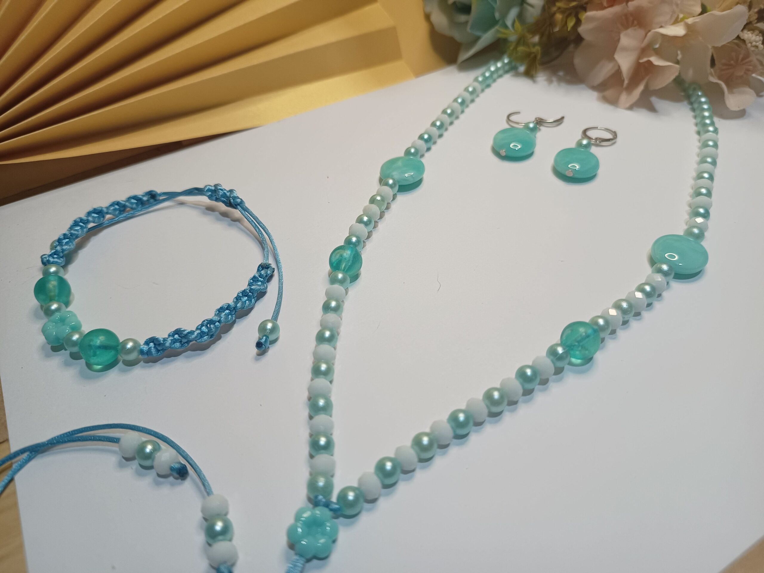 Conjunto Acqua com 3 peças, sendo a 1ª peça um colar gravatinha com 34 cristais na cor brança, pérolas, pastilhas e esferas na cor verde água, 2ª peça Brincos com pastilha e pérolas na cor verde água e base de brinco argola click prateada e a 3ª peça uma pulseira trabalhada em macramê com pérolas, esferas e entremeio iguais a do colar na cor verde água e fecho em macramê ajustável.