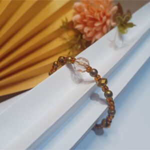 Pulseira mola de arame com cristais dourados, contas metálicas em ouro velho, miçangas marrons e conta central marrom translúcido