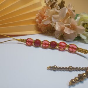 Strap para celular trabalhado em macramê com fio de seda na cor dourada com cristais douradas, contas vermelhas na forma de cubo e contas esféricas na cor vermelha e miçangas em ouro velho