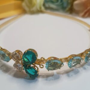 Tiara folheada a ouro 18k com cristais em forma de gota na cor água marinha, com aplicação de 4 cristais formando uma borboleta na cores verde translúcido e incolor